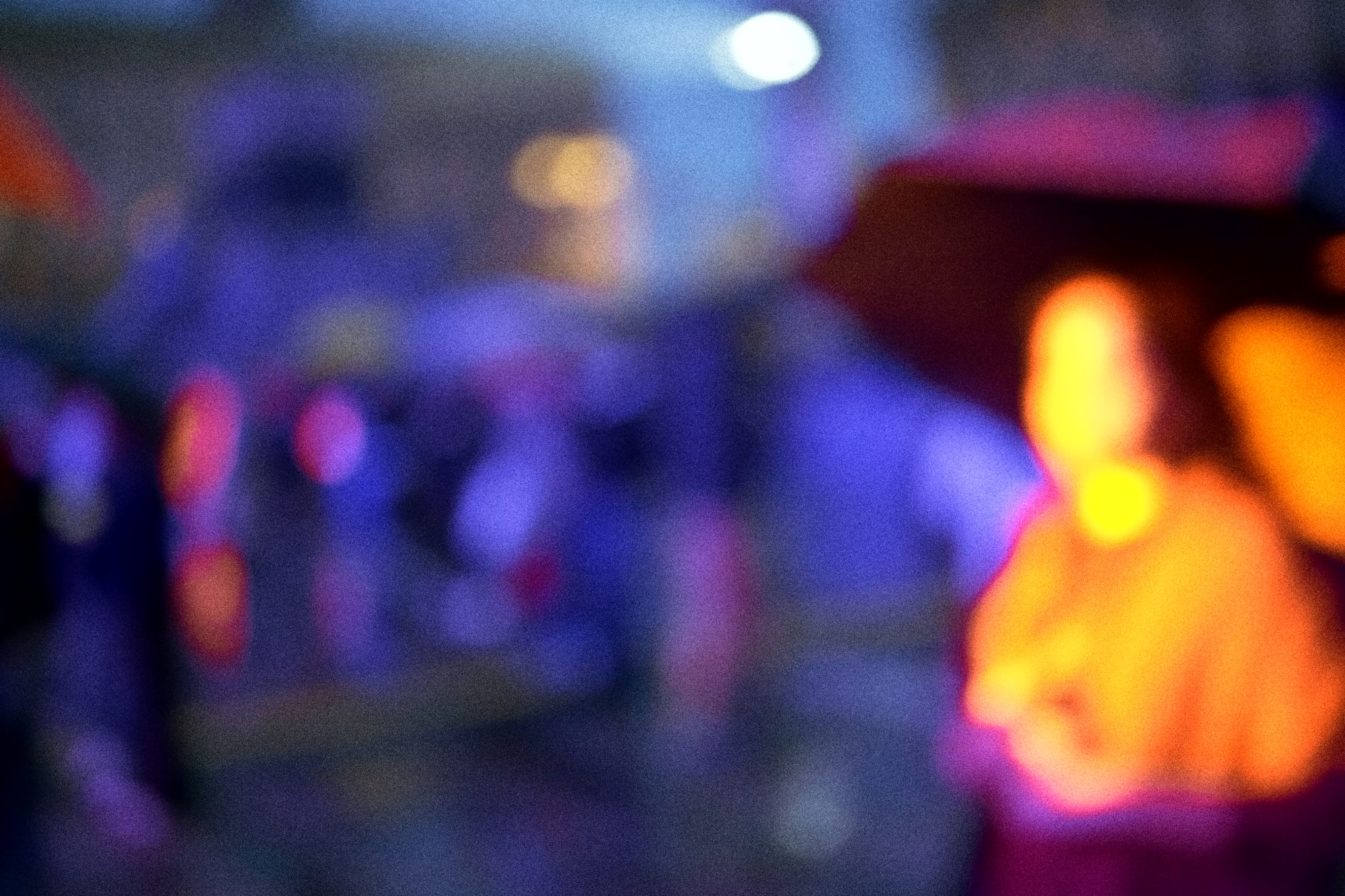 A figure in orange light through blue rain and bokeh.